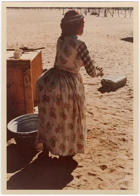 "Misc. prints with no numbers": Woman wearing a dress, standing next to a metal basin