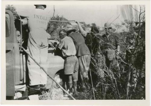 "1950 - 300 series duplicates": Group of men standing next to broken-down expedition truck