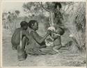 !Ungka (≠Toma's sister), with her daughter, Sa≠gai, sitting on her knees drinking from an ostrich egg shell; Tsamgao (Bau's husband) sitting beside her (print is a cropped image)