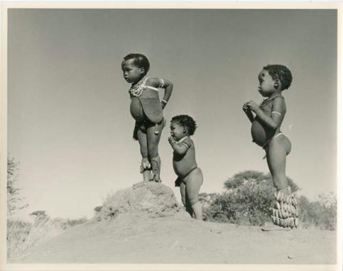 /Gaishay (son of "Gao Medicine" and Di!ai), Bau (daughter of "Crooked /Qui"), and "Little ≠Gao" (son of "/Qui Navel") standing on an ant hill (print is a cropped image)