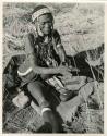 "Old /Gam" sitting and drilling holes in ostrich eggshell beads with her drill (print is a cropped image)