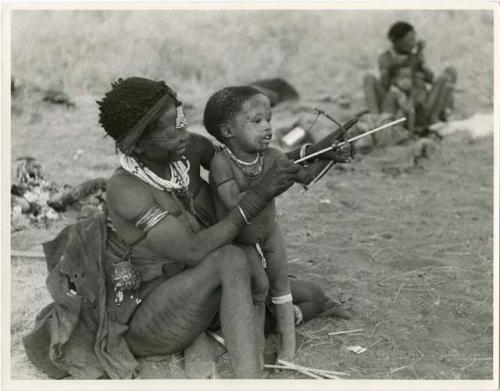 Di!ai showing her son, Debe, how to hold a toy bow and arrow (print is a cropped image)