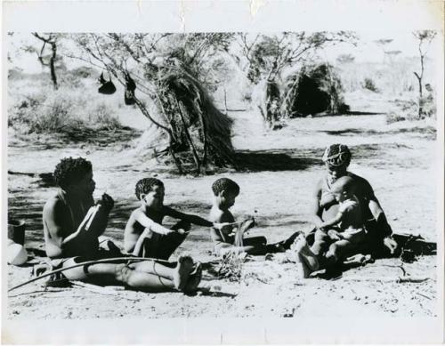 ≠Toma working on arrows and sitting with his family, including Tsamgao, /Gaishay and !U, who is holding Norna on her lap (print is a cropped image)