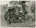 !Ungka (≠Toma's sister), with her daughter, Sa≠gai, sitting on her knees drinking from an ostrich egg shell; Tsamgao (Bau's husband) sitting beside her (print is a cropped image)