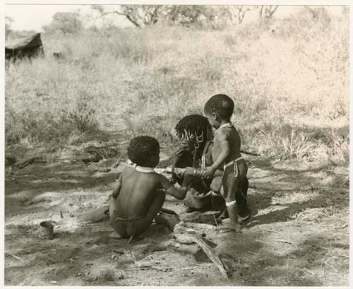 N!ai, eating, and her half-brothers, /Gaishay and Debe, all beside a fire (print is a cropped image)
