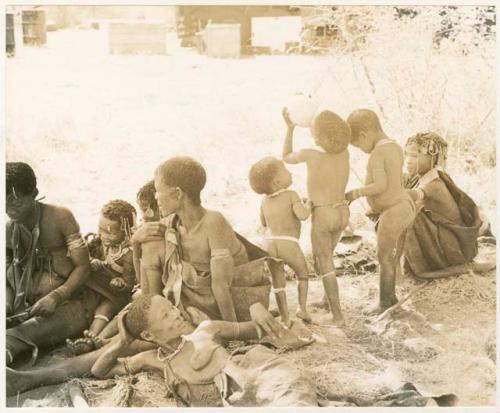 Group of women and children in the shade including Khuan//a, /Gaishay drinking from an ostrich egg, Debe, and Bau ("Crooked /Qui's" daughter) (print is a cropped image)