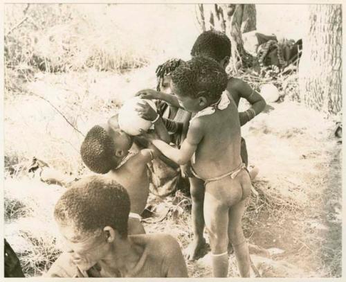 Group of unidentified children including /Gaishay helping his younger brother, Debe, take a drink from an ostrich eggshell (print is a cropped image)