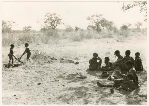 /Gaishay and Bau carrying the cooked wildebeest head away from a group of women and children (print is a cropped image)