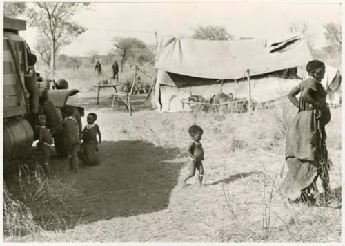 Children playing around the expedition truck while Di!ai and Debe walk away; the expedition camp is in the background (print is a cropped image)