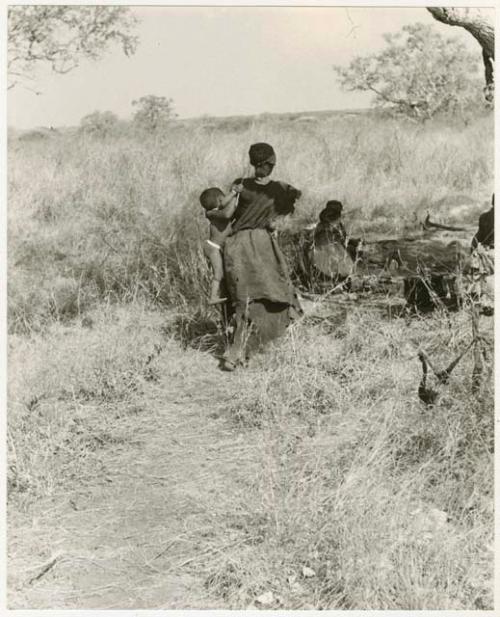 Di!ai seen from the back, carrying Debe against her side (print is a cropped image)