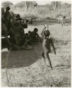 Ju/'hoan boy holding a can on his head walking toward a group of children around the expedition truck (print is a cropped image)
