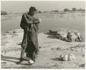 Woman, standing, gathering her filled ostrich egg shells (print is a cropped image)
