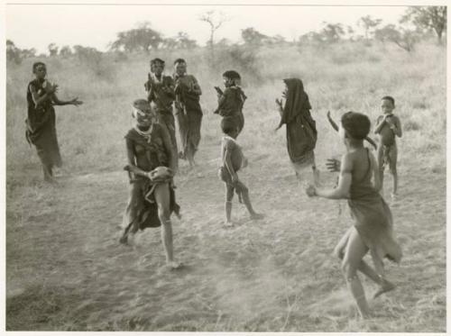 Girls playing N!owa t/ama (melon tossing game) / tamah n!o’an (ball game); an unidentified visiting girl catches the melon; other children in the background (print is a cropped image)