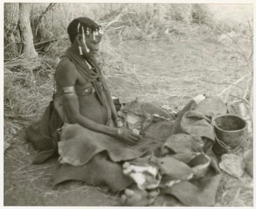 Woman pounding bone and red powder in her kaross with a stone (print is a cropped image)