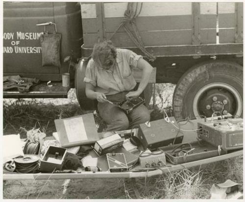 Elizabeth Marshall Thomas sitting in front of the expedition truck monitoring the recorder with equipment laid out in front of her (print is a cropped image)
























