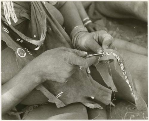 Woman's hands sewing beads onto a leather strip, close-up (print is a cropped image)