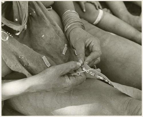 Woman's hands sewing beads onto a leather strip, close-up (print is a cropped image)