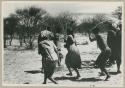 [No folder title]: People performing the Eland Dance, with Twi imitating the sideways motion of an eland's hind legs and playing up to ǂKxoba (from color slide 2001.29.8657)