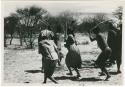 [No folder title]: People performing the Eland Dance, with Twi imitating the sideways motion of an eland's hind legs and playing up to ǂKxoba (from color slide 2001.29.8657)