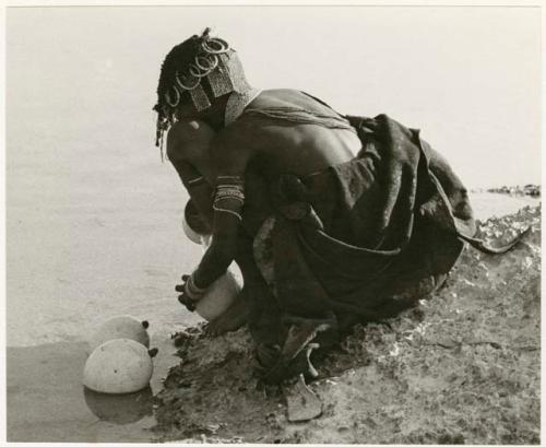 Girl filling an ostrich eggshell, seen from behind (print is a cropped image)