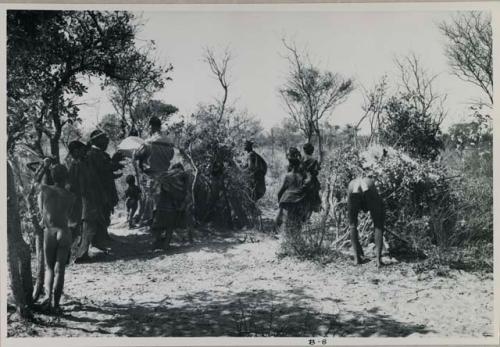 [No folder title]: Group of women performing a menstruation ceremony, an expedition member recording sound; a man bent over, seen from behind