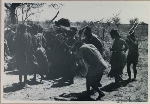 [No folder title]: Group of people performing the Eland Dance; group of women clapping; men holding wooden horns to their heads
