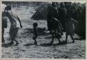 [No folder title]: Group of people performing the Eland Dance; group of women clapping; children following the men holding wooden horns to their heads