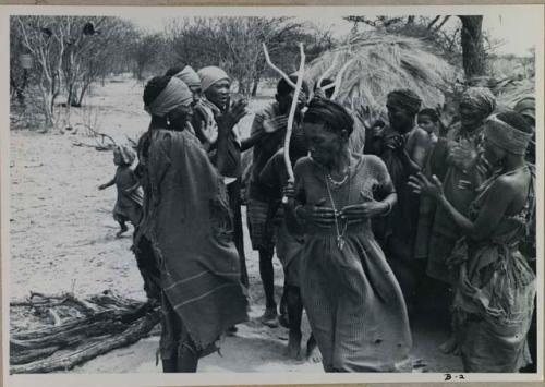 [No folder title]: Group of people performing the Eland Dance; group of women clapping as a line of men holding wooden horns to their heads passes by