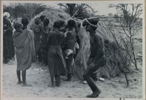 [No folder title]: Group of people performing the Eland Dance; group of women clapping; man with wooden horns strapped to his head

