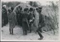 [No folder title]: Group of people performing the Eland Dance; group of women clapping; man with wooden horns strapped to his head

