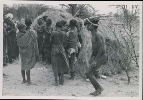 [No folder title]: Group of people performing the Eland Dance; group of women clapping; man with wooden horns strapped to his head

