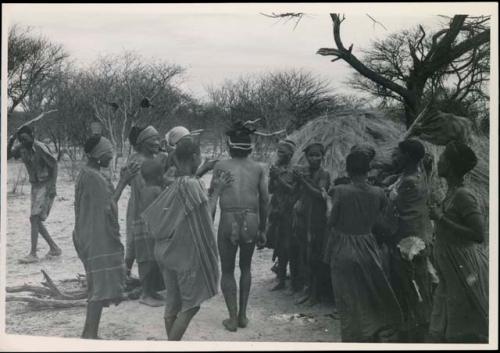 [No folder title]: Group of people performing the Eland Dance; group of women clapping; men with wooden horns on their heads

