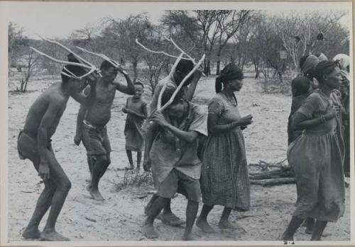 [No folder title]: Group of people performing the Eland Dance; group of women clapping; men with wooden horns on their heads

