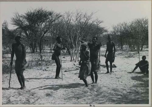 Tomku, /Gaishay, and a group dancing, /Gaishay's arms over Tomku; people sitting to the side