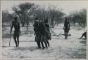 Tomku, /Gaishay, and a group dancing, /Gaishay's arms over Tomku and another woman; people sitting to the side