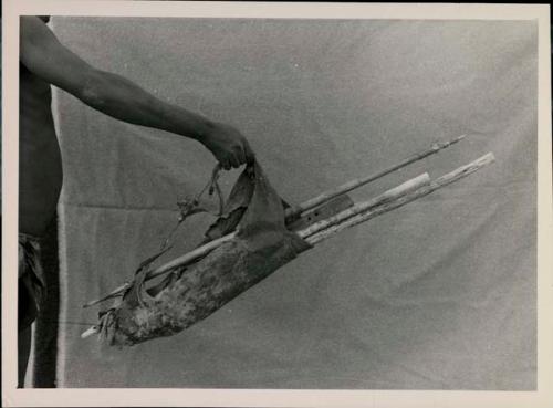 [No folder title]: Hunting bag containing quiver and sticks, held against a sheet






