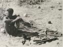 [No folder title]: Oukwane sitting, with his possessions on the ground next to him





