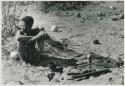 [No folder title]: Oukwane sitting, with his possessions on the ground next to him





