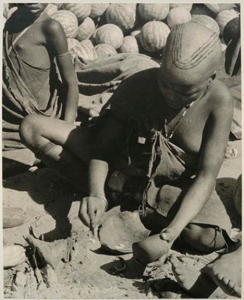 [No folder title]: Girl pounding tsama melon seeds in a piece of gourd used as a receptacle
