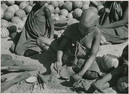 [No folder title]: Girl pounding tsama melon seeds in a piece of gourd used as a receptacle
