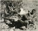 [No folder title]: Oukwane and !Gai reclining; /Twikwe passing a pipe to Oukwane
