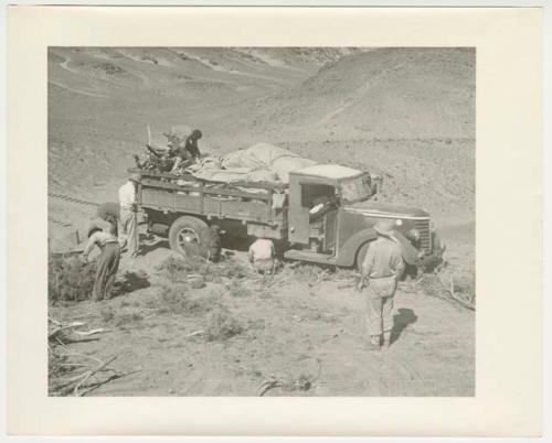 "1950's 400 series": Expedition members putting brush under wheels of truck and retrieving something from the load (print is a cropped image)