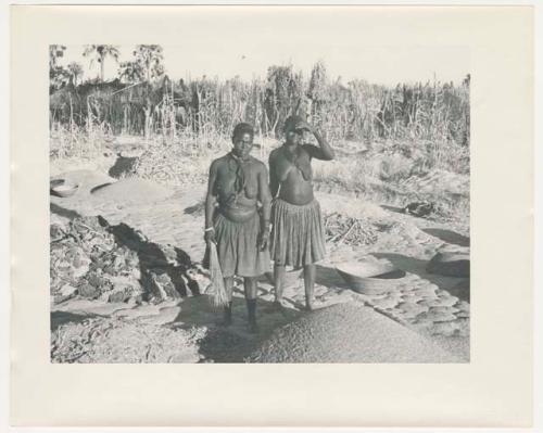 "Glossy duplicates of / 1950 Merl La Voy prints / 400 series": Two women standing next to piles of grain (print is a cropped image)