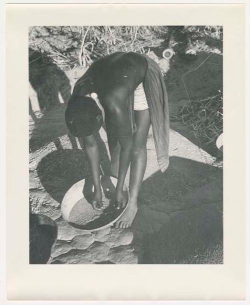 "Glossy duplicates of / 1950 Merl La Voy prints / 400 series": Woman leaning over a basket of grain (print is a cropped image)