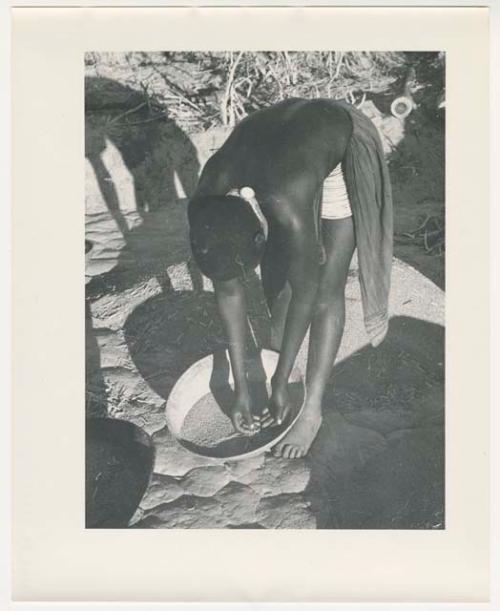 "Glossy duplicates of / 1950 Merl La Voy prints / 400 series": Woman leaning over a basket of grain (print is a cropped image)