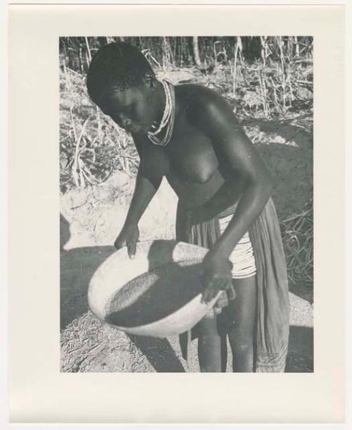 "Glossy duplicates of / 1950 Merl La Voy prints / 400 series": Woman standing and holding a basket of grain (print is a cropped image)