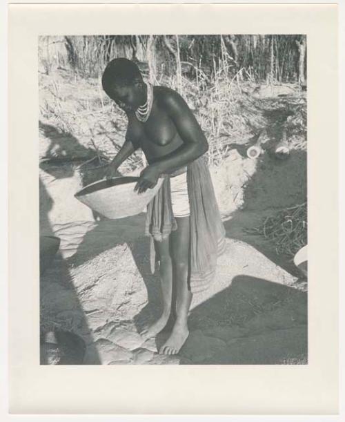 "Glossy duplicates of / 1950 Merl La Voy prints / 400 series": Woman standing and holding a basket of grain (print is a cropped image)