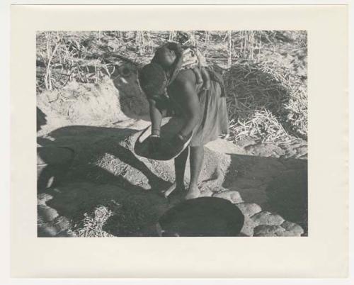 "Glossy duplicates of / 1950 Merl La Voy prints / 400 series": Woman carrying a baby on her back and holding a basket of grain (print is a cropped image)