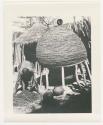 "1950 '400 Series' / 87 B/W prints (some duplicates) / Ovamboland": Woman working and leaning over, and another woman standing at the top of a storage basket (print is a cropped image)