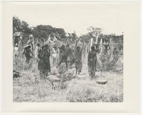 "1950 '400 Series' / 87 B/W prints (some duplicates) / Ovamboland": Group of people standing, with baskets of grain on the ground near them (print is a cropped image)